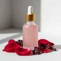 Rose Hibiscus Hydrating Serum in a frosted glass dropper bottle with gold top surrounded by rose petals and hibiscus flowers